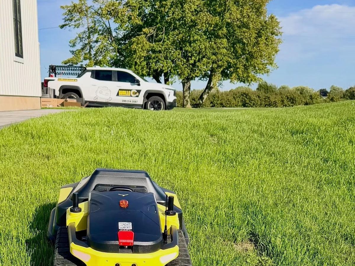 A Yarbo robotic mower cutting grass on an Ontario property with a WALLE Corp. branded truck parked behind