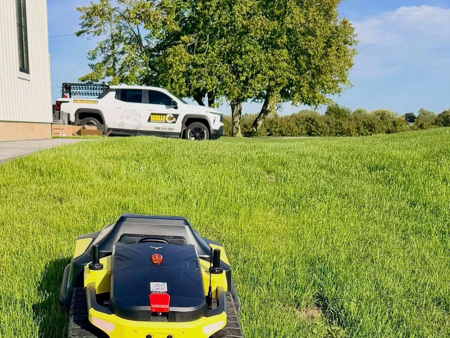 A Yarbo robotic mower cutting grass on an Ontario property with a WALLE Corp. branded truck parked behind